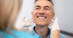 Doctora de la clínica Simetría Dental examina el implante dental de un paciente sonriente